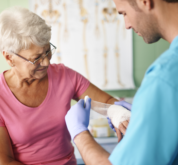 Clinician carefully bandaging an older patient's hand during a wound-care visit